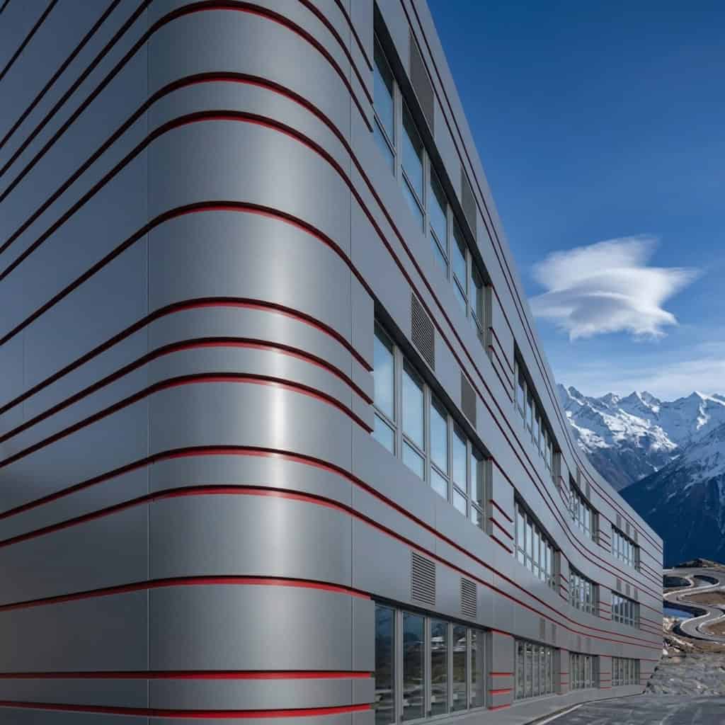 Ein modernes Gebäude mit gebogener Fassade aus Aluverbundplatten vor einer Bergkulisse